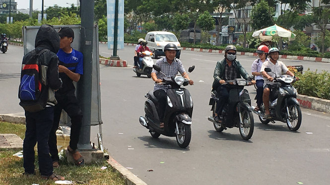 Hai thanh niên phát tờ rơi vòng xoay Nguyễn Thái Sơn, quận Gò Vấp tranh thủ núp sau tâm bảng hiếm hoi trên đường để tránh nắng - Ảnh Tự Trung